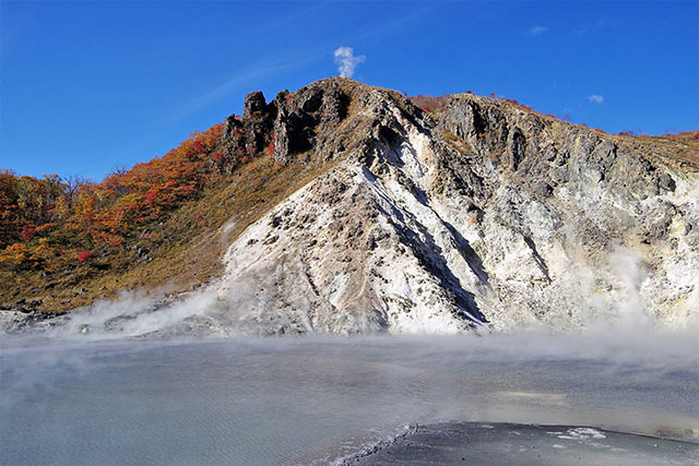 灰黒色をしている「大湯沼」と、噴煙があがる日和山