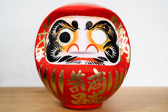 A typical Daruma Doll with all the classic markings on its face including cranes for eyebrows and turtles for facial hair. These two animals have long represented longevity in East Asian culture.